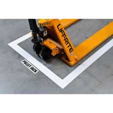 Brady vinyl aisle marking tape applied to the floor reading "pallet jack" framing where a pallet jack is stored.