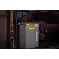A large piece of electrical equipment stands on the floor and is marked with many labels. 
