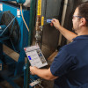 A person standing in front of industrial machinery and piping holds a lockout procedure in his left hand and a blue valve tag attached to a valve in their right hand.