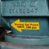 Primer plano de una etiqueta de flecha amarilla en una máquina con el texto “Normal Set Point 185 Degrees F, 240 psi."