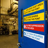 Una puerta azul abierta con cuatro etiquetas diferentes aplicadas en ella, que lleva a la puerta de una planta industrial.